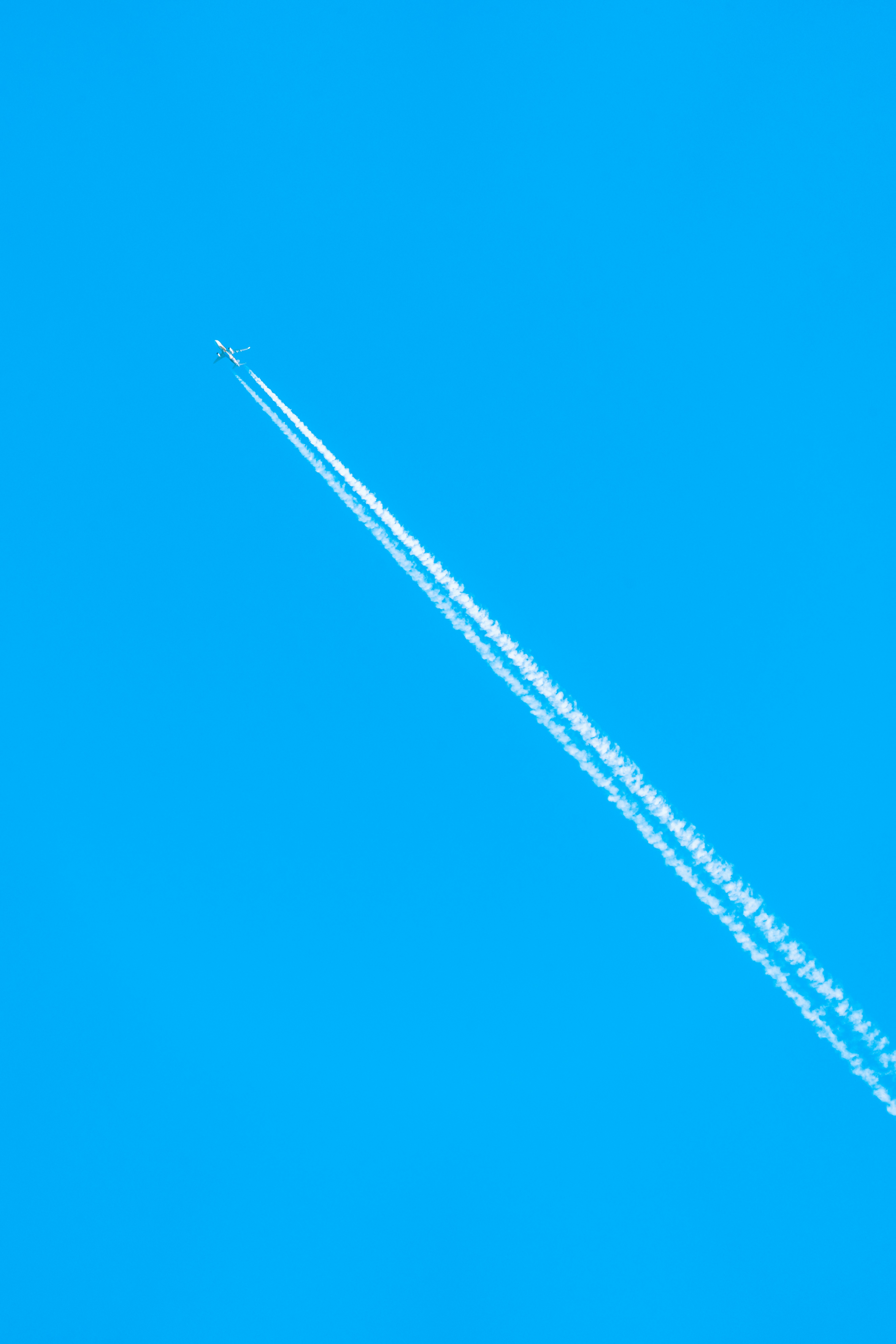 White plane flying above and leaving a contrail in a bright blue sky.